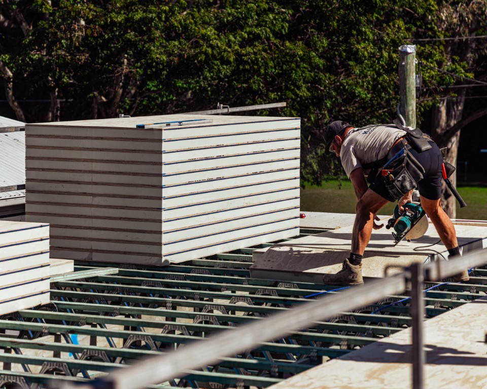Installer with a drill beside a stack of Platinum "R" Floor on the steel joists
